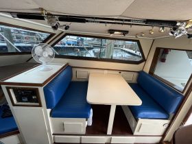 Interior view of a boat's cabin featuring comfortable blue seating and a fan, perfect for relaxing while on the water.