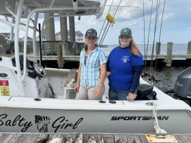 Two women pose on the deck of the 'Salty Girl' fishing boat, showcasing their catch and ready for a day on the water.