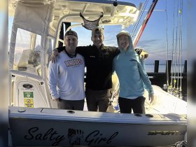 A group of friends poses together on the deck of the 'Salty Girl' boat, ready for a fishing adventure at sunset. Perfect for capturing memorable moments on the water.
