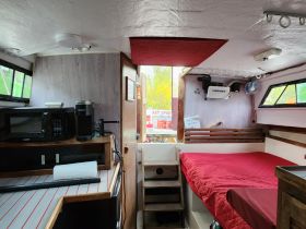 Interior view of a cozy boat cabin featuring a sleeping area, kitchenette, and ample storage — perfect for comfortable overnight trips on the water.