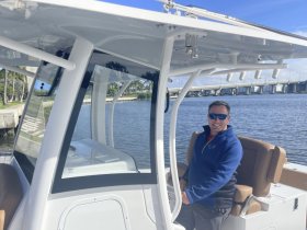 A smiling man sits at the helm of a well-equipped boat, showcasing the comfortable seating and modern console — perfect for a day on the water.