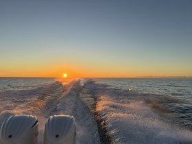 A stunning sunset view from the back of a boat, showcasing the wake and tranquil waters — perfect for evening cruises.