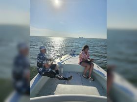 A couple enjoys a sunny day fishing on a boat, surrounded by shimmering water — a perfect setting for a relaxing day on the water.