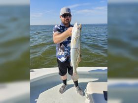 A proud angler displays his impressive catch while fishing on the water, showcasing the thrill of outdoor adventures.