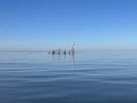 A serene view of calm waters under a clear blue sky, featuring a distant structure. The image lacks clarity and detail.