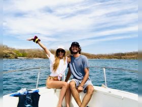A joyful couple poses on the bow of a boat, enjoying a sunny day on the water — perfect for romantic getaways or fun outings.