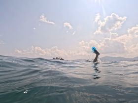 A snorkeler's fin splashes in the water, capturing the excitement of underwater exploration against a scenic backdrop of clouds and distant mountains.