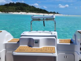 A close-up view of the helm and console area of a boat, showcasing the sleek design and functionality, with a stunning turquoise water backdrop.