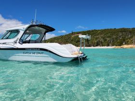 A sleek speedboat named 'Catch My Drift' anchored in crystal-clear waters, showcasing its elegant design against a lush tropical backdrop.