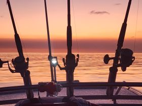 A serene sunset view from a fishing boat, showcasing fishing rods against a tranquil sea — perfect for capturing the essence of a peaceful evening on the water.