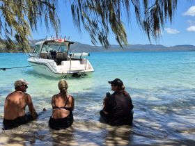 A group enjoys a relaxing moment on the beach, with a boat anchored nearby, perfect for fishing adventures and beachside fun.