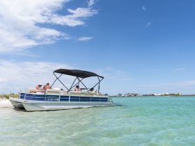 A lively group enjoys a day on a pontoon boat anchored near the beach, perfect for swimming and relaxation in the sun.