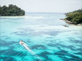An aerial view of a boat cruising through stunning turquoise waters, surrounded by lush greenery and rocky coastlines — a perfect scene for exploring tropical destinations.
