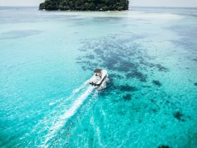 An aerial view of a speedboat cruising through crystal-clear turquoise waters, showcasing the beauty of a tropical paradise.