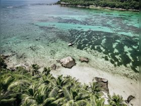 Aerial view of a boat anchored in crystal-clear turquoise waters, surrounded by lush tropical vegetation and rocky shores, showcasing a serene coastal landscape.