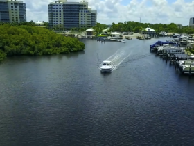 Aerial view of a speedboat cruising through calm waters, surrounded by lush greenery and modern buildings, showcasing a serene boating experience.