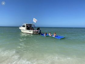 A group of young girls enjoys a fun day on the water, relaxing on a floating mat near a boat, perfect for summer adventures and water activities.