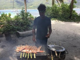 A chef grills fresh seafood on a barbecue, creating a delicious meal in a tropical setting — perfect for catering on boat trips or beach outings.