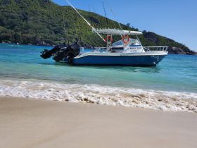A fishing boat named 'BOUT TIME' is docked in clear turquoise waters, showcasing a serene beach setting perfect for fishing trips or leisure outings.