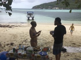A lively beach scene featuring a couple enjoying food and drinks while a child plays nearby — perfect for family gatherings and beach outings.