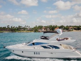 A stunning yacht cruising through clear waters, showcasing its elegant design against a backdrop of lush greenery and coastal homes.