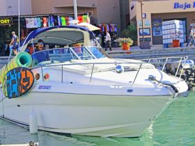 A sleek speedboat docked at the marina, featuring a vibrant surfboard and a captain at the helm, perfect for water adventures.