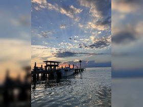 A serene sunset view featuring a boat docked at a pier, with a person visible enjoying the tranquil waterscape — perfect for capturing the beauty of evening boat outings.