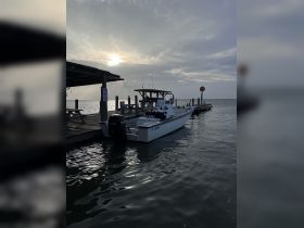 A serene view of a fishing boat docked at a pier, with the sun setting in the background, perfect for a day on the water.