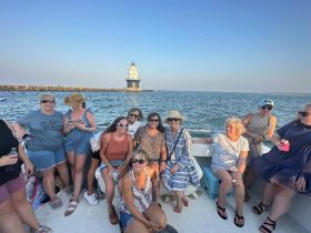 A lively group of friends enjoys a fun day on the water, celebrating together aboard a boat with a scenic lighthouse in the background.