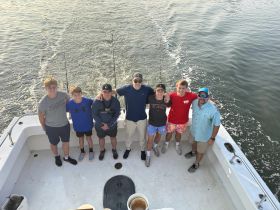 A cheerful group of friends poses on the deck of a fishing boat, ready for a day of adventure on the water. Perfect for capturing memories of fishing trips and camaraderie.