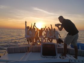 A lively group celebrates at sunset on a boat, capturing the moment with joyful poses and smiles — perfect for unforgettable memories on the water.