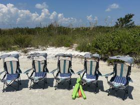 A set of beach chairs and pool noodles arranged on the sand, perfect for a relaxing day by the water or family fun in the sun.