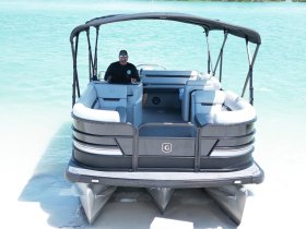 A sleek pontoon boat is docked in shallow waters, with a captain at the helm, showcasing the perfect vessel for leisurely outings on the water.