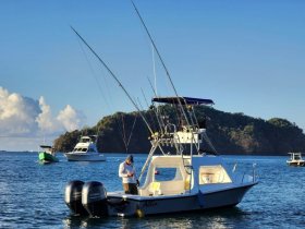 A fishing boat is anchored in calm waters, with a fisherman preparing for the day. The scenic backdrop features lush greenery, perfect for a day of fishing adventures.