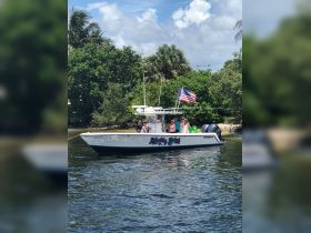 A lively group enjoys a day on the water aboard a boat named 'Weekly Bich,' surrounded by lush greenery and clear skies — perfect for fun-filled outings.