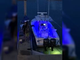 Two individuals stand by a brightly lit boat at night, creating a vibrant atmosphere perfect for evening fishing trips or dockside gatherings.