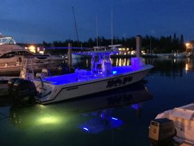 A stunning night view of a Contender boat illuminated with blue lights, docked peacefully at the marina, showcasing its sleek design against the tranquil waters.