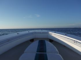A serene view from the bow of a boat cruising over calm waters, showcasing the vast ocean and clear sky — perfect for a day on the water.