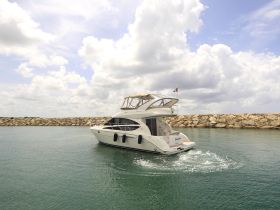 A stunning yacht glides through calm waters, showcasing its elegant design against a backdrop of fluffy clouds and a rocky shoreline.