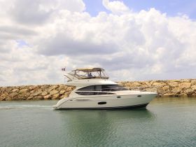 A stunning yacht navigates through calm waters, showcasing its elegant design against a backdrop of rocky shores and a cloudy sky.
