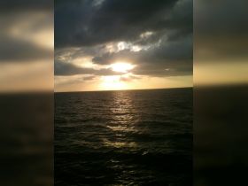 A scenic view of the ocean at sunset, with clouds reflecting the golden light, creating a serene atmosphere.