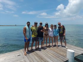 A cheerful group poses together on a dock by the clear turquoise waters, capturing a memorable moment during their beach adventure.