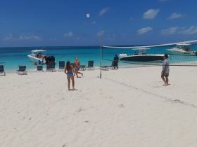A lively beach scene with friends playing volleyball while boats are anchored nearby, capturing the essence of fun and relaxation in a tropical paradise.