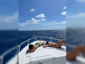 Two friends relax and sunbathe on the bow of a boat, enjoying a beautiful day on the ocean — perfect for a fun day out on the water.