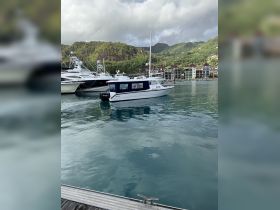 A serene view of a boat named 'Kastler' docked in a picturesque harbor, surrounded by lush green hills and luxury yachts.