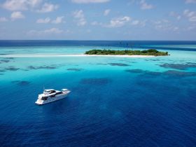 A stunning aerial view of a luxurious yacht cruising through crystal-clear turquoise waters, with a picturesque island in the background — perfect for tropical getaways and island hopping adventures.