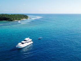 A stunning aerial view of a luxurious yacht cruising through crystal-clear waters, surrounded by lush greenery — perfect for showcasing boating adventures.