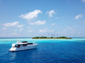 A stunning aerial view of a luxurious yacht cruising through crystal-clear turquoise waters, with a picturesque island in the background, perfect for tropical getaways.