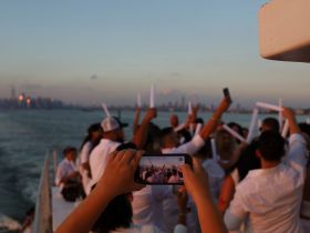 A lively group celebrates on a boat at sunset, capturing the moment with phones — perfect for unforgettable party experiences on the water.
