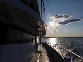 A stunning view of a boat's side against a backdrop of a shimmering sunset over the water, perfect for showcasing the beauty of maritime adventures.
